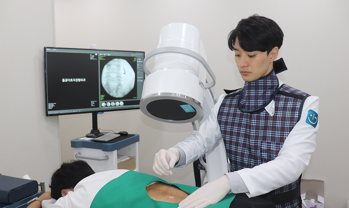 원장이 C-arm 영상을 보며 척추 주사 시술을 하는 장면